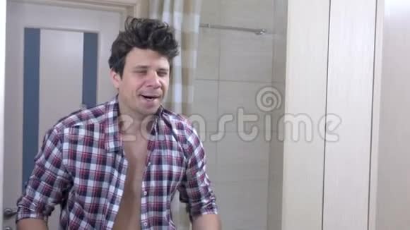 早上一个宿醉的困乏男人在浴室里打哈欠系好衬衫整理好自己视频的预览图
