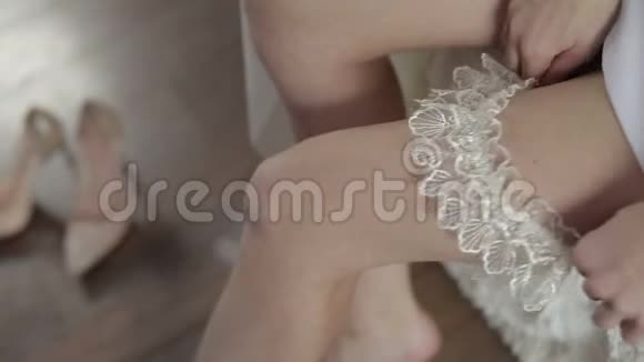 美丽可爱的新娘穿着睡衣把吊袜带装在腿上结婚的早晨特写镜头视频的预览图