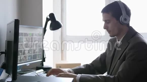 成功的商人戴着耳机坐在办公桌前在全景窗口的电脑上工作3840x2160视频的预览图