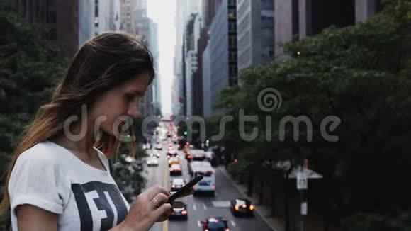 年轻美丽的女性站在纽约交通道路附近的桥上使用智能手机的肖像视频的预览图