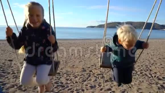 一个三岁的男孩和一个六岁的女孩在一个阳光明媚的早晨在海岸上荡秋千视频的预览图