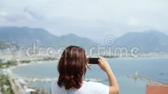 穿着白色连衣裙的女游客在智能手机上从高处拍摄城市视频的预览图