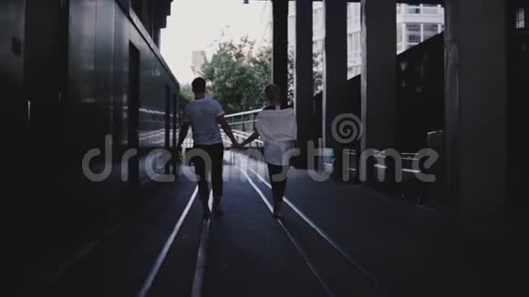 慢镜头后视不可辨认的男人和女人一起走双手在大黑暗的城市桥下的铁轨上视频的预览图
