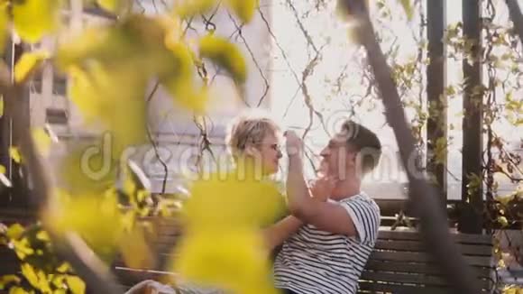 慢动作轻松微笑的年轻男女在秋天公园的长凳上聊天享受外面美丽的晴天视频的预览图