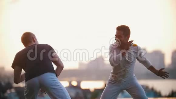 很强壮的男人表现出了卡普伊拉的舞蹈技巧在草地上战斗在日落时微笑视频的预览图