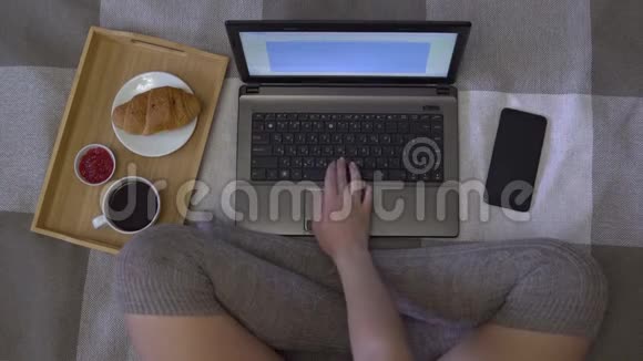 头顶镜头女孩坐在床上用笔记本电脑工作看着手机上的收入表视频的预览图