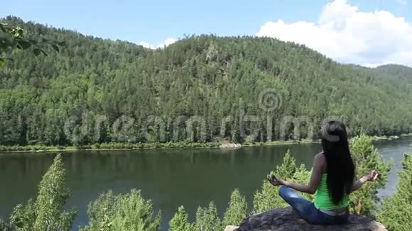 女人以莲花的姿势冥想在山顶上的岩石上做瑜伽视频的预览图