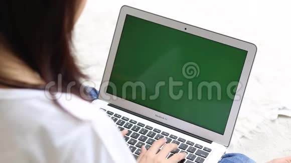 美丽的亚洲年轻女子躺在床上卧室里用笔记本电脑显示绿色屏幕视频的预览图