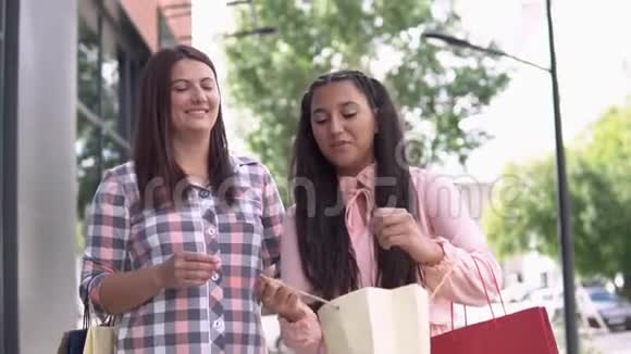 两个穿着漂亮衣服的漂亮女孩拿着购物袋在商场附近购物后去慢动作高清高清视频的预览图