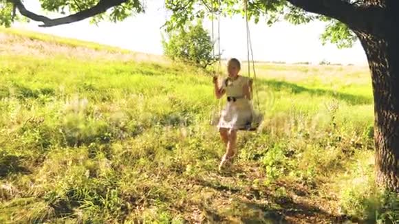 快乐的女孩长发在夏天的橡树下摇摆穿着白色的裙子笑着视频的预览图