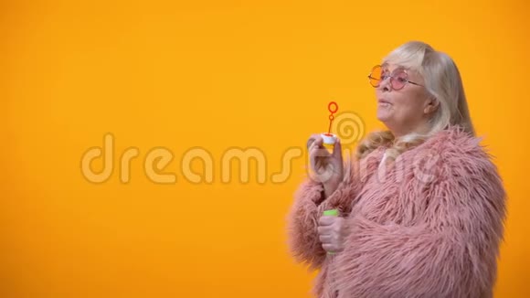 穿着有趣的粉红色外套和圆墨镜做肥皂泡的积极的老年妇女视频的预览图