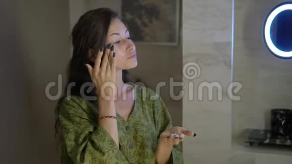 穿着睡衣的漂亮年轻女士站在酒店浴室里按摩脸上涂着奶油视频的预览图