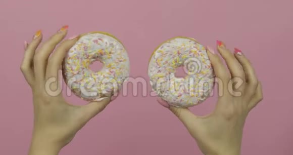 女人的手拿着两个白色的美味的洒在粉红色背景上的甜甜圈视频的预览图