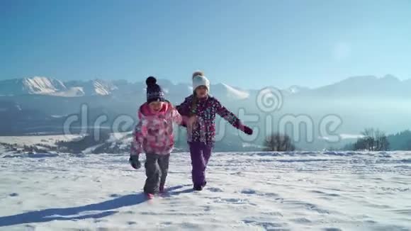 穿着户外服装的孩子们在雪地上奔跑阳光下背景着美丽的山脉视频的预览图