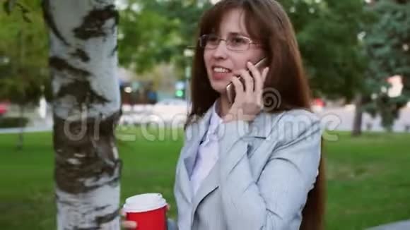 女商人戴着浅色西装的眼镜上班女孩喝咖啡在智能手机上讲话视频的预览图