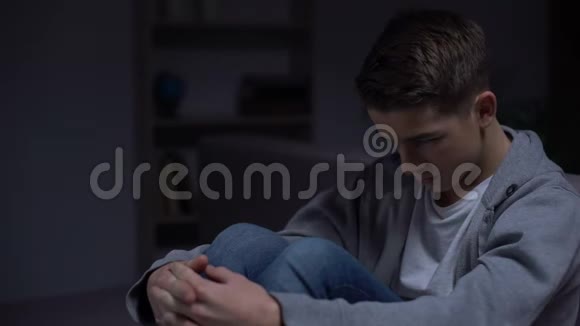 沮丧的十几岁男孩坐在黑暗的房间里与父母的误解视频的预览图