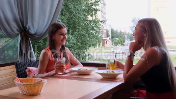 两个时髦的酷女孩朋友金发和黑发在咖啡馆喝鸡尾酒视频的预览图