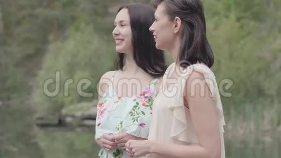 两位迷人的年轻女子穿着夏装站在岩石的顶端看着令人惊叹的自然景观视频的预览图