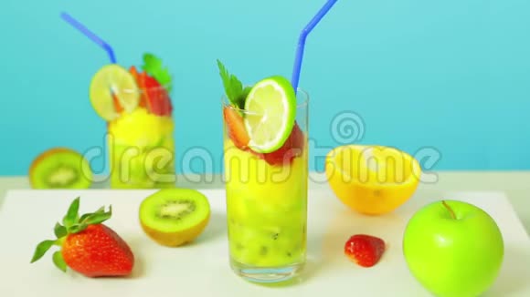 水果鸡尾酒在一个玻璃装饰石灰与蓝色吸管在蓝色背景靠近猕猴桃草莓苹果视频的预览图