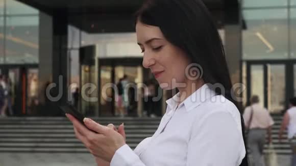 成功的商务女性穿着白色衬衫使用智能手机微笑着在城市视频的预览图