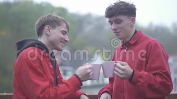 两个穿红色夹克的男人喝着咖啡杯微笑着朋友一起在户外度过时光视频的预览图