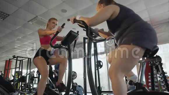 胖女士骑着固定的自行车工作看着瘦女士比较视频的预览图