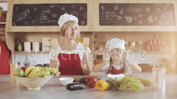妈妈和小女儿在厨房打扮成专业厨师看着镜头微笑他们持有视频的预览图