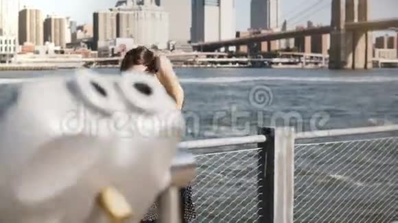 快乐轻松微笑留着长发的白种人女孩在阳光明媚的日子里沿着曼哈顿的天际线散步在电话中交谈视频的预览图