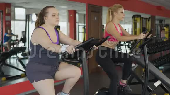 有趣的肥胖女士在健身俱乐部骑着固定自行车骑得很快动机视频的预览图