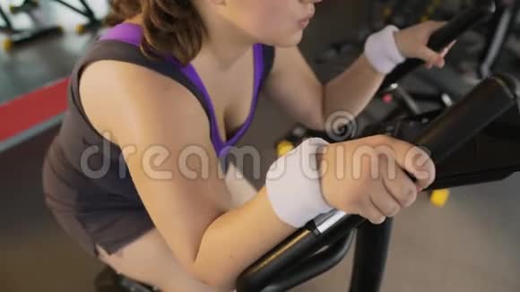 心脏锻炼丰满的女人骑着固定的自行车和出汗运动视频的预览图