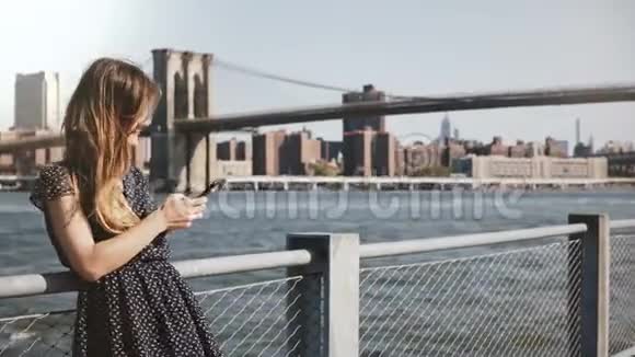 美丽的微笑白种人女孩长发站在纽约著名的天际线景观使用智能手机走开视频的预览图