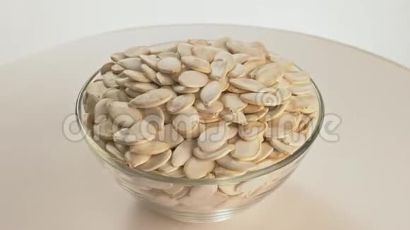 坚果未剥皮南瓜种子旋转是在一个桌子在一个盘子在白色背景上的透明盘子中提供小吃视频的预览图