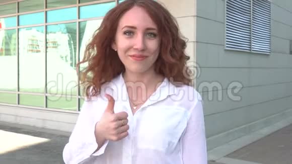 年轻漂亮的红发女孩在户外街头散步在公园里竖起大拇指视频的预览图