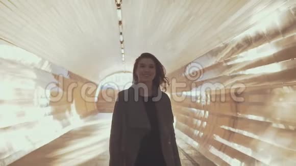 戴太阳镜的漂亮女孩穿着外套穿过阳光明媚的隧道日落时分视频的预览图