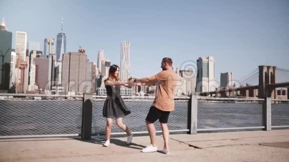 快乐的欧洲情侣在纽约著名的曼哈顿天际线景观附近做一个快乐的旋转舞蹈牵手慢动作视频的预览图