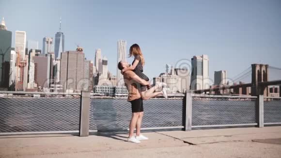 快乐的白种人男人抱着他的女朋友在纽约著名的布鲁克林桥景观慢动作微笑视频的预览图