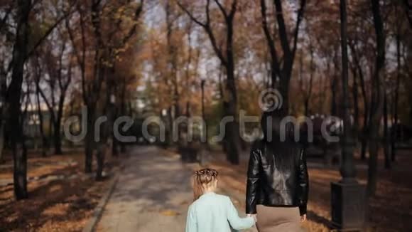 妈妈和女儿正沿着一条布满秋黄树叶的大道走着一家人在城市公园散步视频的预览图