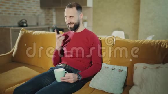长胡子的帅哥在手机上聊天在家喝咖啡或茶视频的预览图