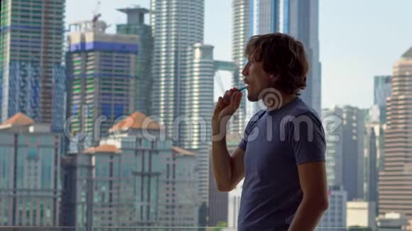 年轻人刷牙站在阳台上看到一个充满摩天大楼的市中心视频的预览图