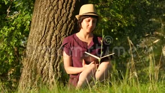 在公园看书的年轻女学生文化阅读教育坐在树旁的女孩摄像机移动视频的预览图