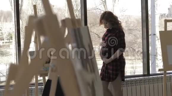 美丽的孕妇站在艺术工作室的窗户附近视频的预览图