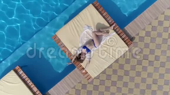夏季身着泳装的年轻女孩的鸟瞰景观就在泳池附近的露台上那里有蓝色美丽的水视频的预览图