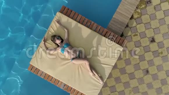 夏天穿着蓝色泳衣和眼镜的漂亮女孩躺在游泳池附近视频的预览图