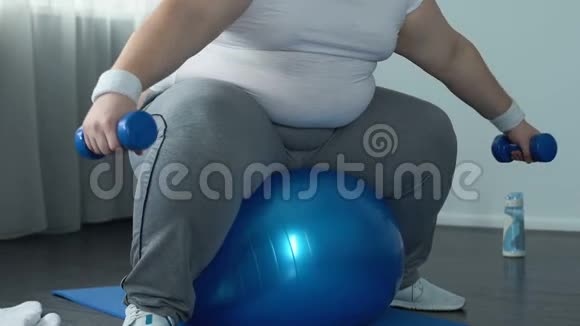 穿着运动服的男运动员举起哑铃坐在健身球上减肥视频的预览图