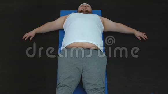 胖乎乎的年轻人在家训练后伸展垫子观看最高的风景健康活动视频的预览图