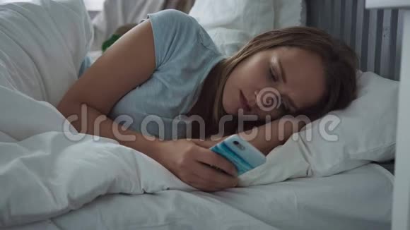 悲伤的女人躺在床上用智能手机试图入睡视频的预览图