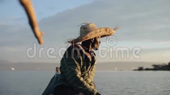 黎明时分戴着草帽的非洲年轻人坐在摩托艇上看着海上的帆船视频的预览图