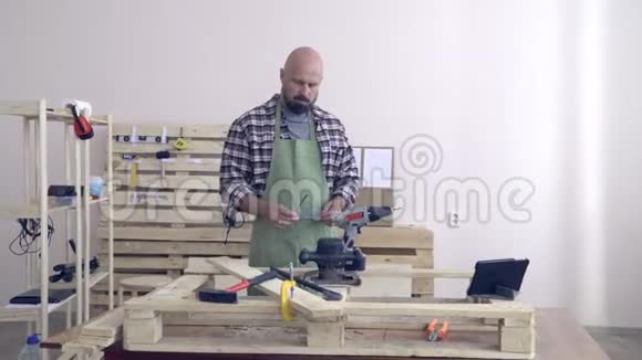 一位50岁的老人穿着格子法兰绒衬衫画着工作室里一位穿着工作服的工匠的画像上面有一个小玩意视频的预览图