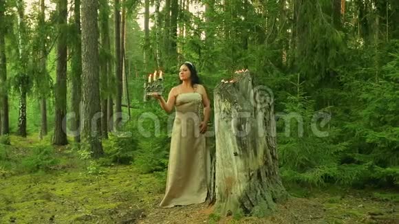 神秘的森林仙女站在一个有蜡烛的大树桩旁手里拿着一个燃着蜡烛的烛台视频的预览图