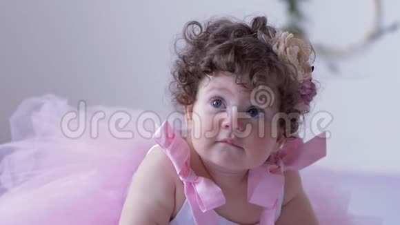 孩子们拍照环节一个大眼睛的小女孩一头卷发穿着粉色连衣裙在白色的摄影棚里摆姿势视频的预览图